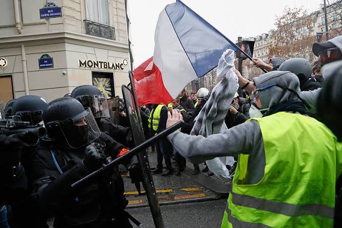 Yellow-vest demonstrators with a French flag facing riot police