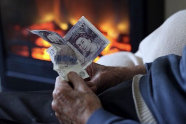 Hands holding British pound banknotes beside a fireplace